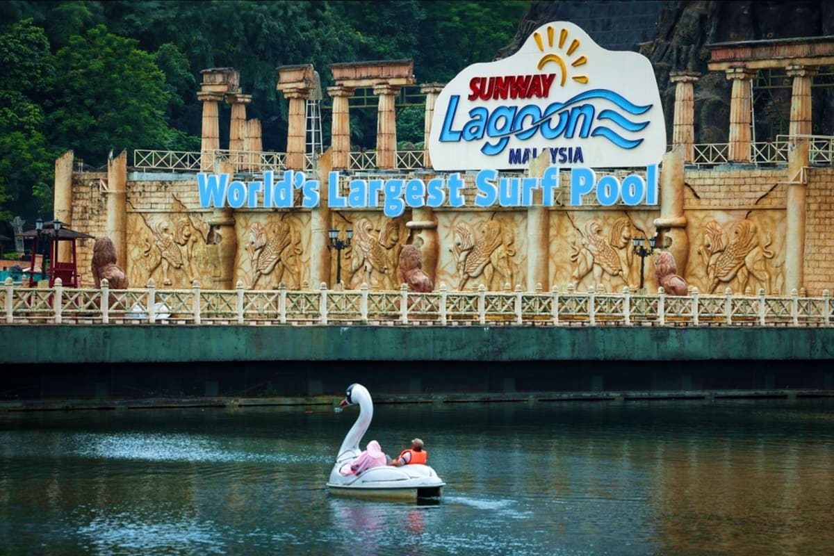 Swan-shaped paddle boat on lagoon in front of Sunway Lagoon Malaysia theme park entrance sign with ancient temple-style archi