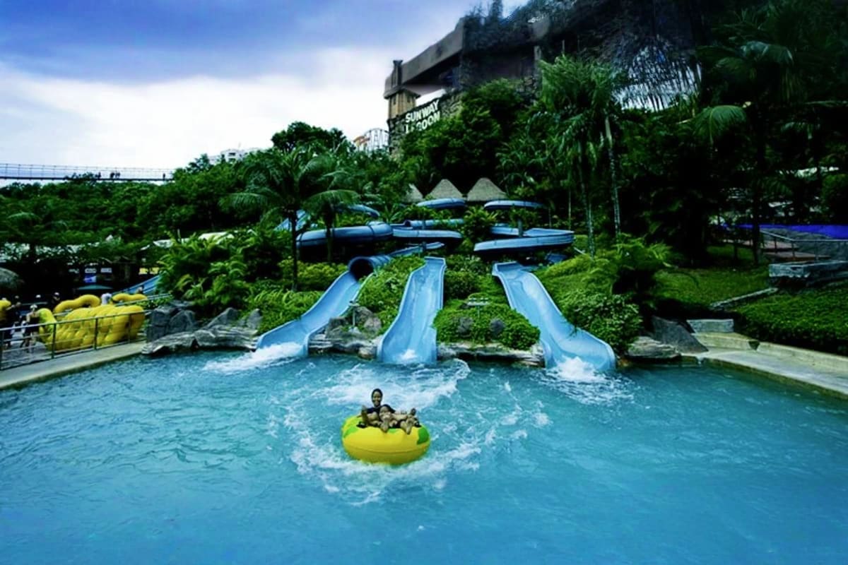 Family enjoying yellow raft ride on blue water with three blue water slides and tropical landscaping at Sunway Lagoon theme p
