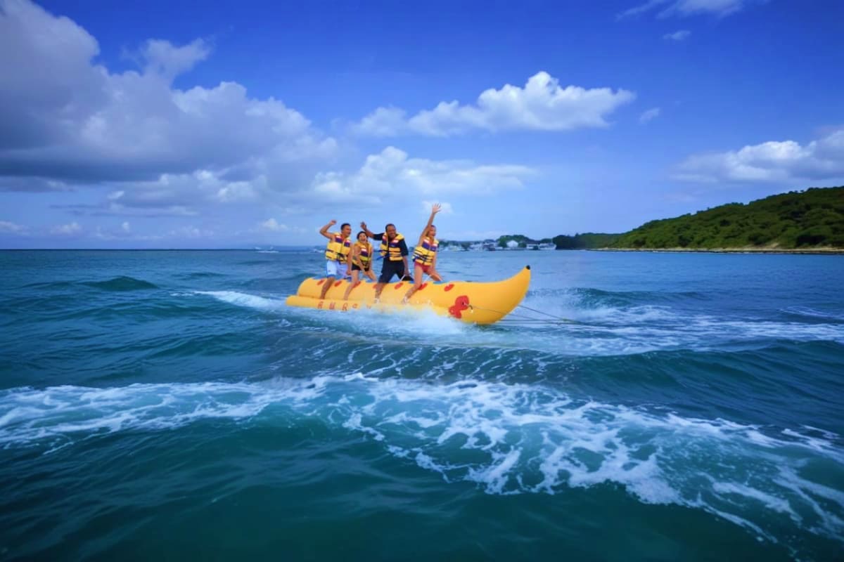 Group of people riding yellow banana boat on ocean waves with blue sky and forested coastline in background