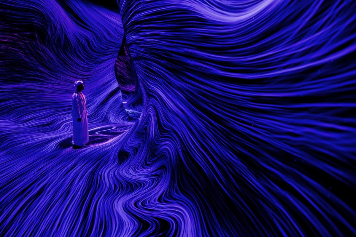 Person standing in immersive digital art installation with flowing purple and blue wave patterns surrounding them in TeamLab
