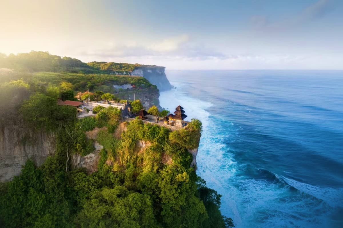 Uluwatu Temple perched on dramatic clifftops overlooking turquoise ocean waters with lush vegetation and traditional Balinese