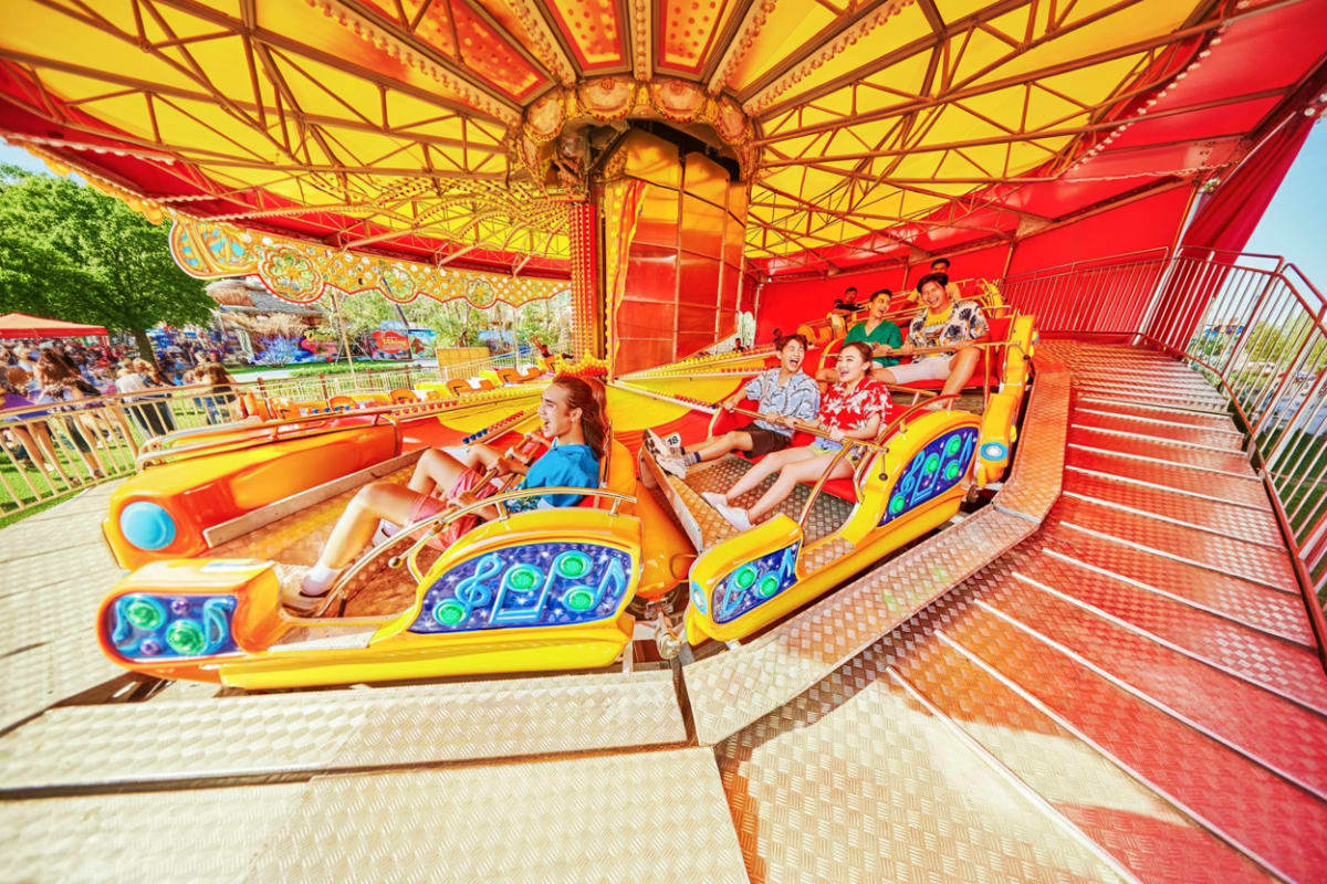VinWonders Grand Park Ho Chi Minh Children riding colorful yellow and orange dragon-shaped roller coaster cars under red and gold carnival canopy at VinWonders
