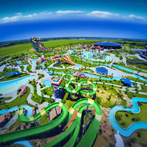 Aerial view of VinWonders theme park with green roller coasters, blue water rides, and colorful attractions surrounded by gre