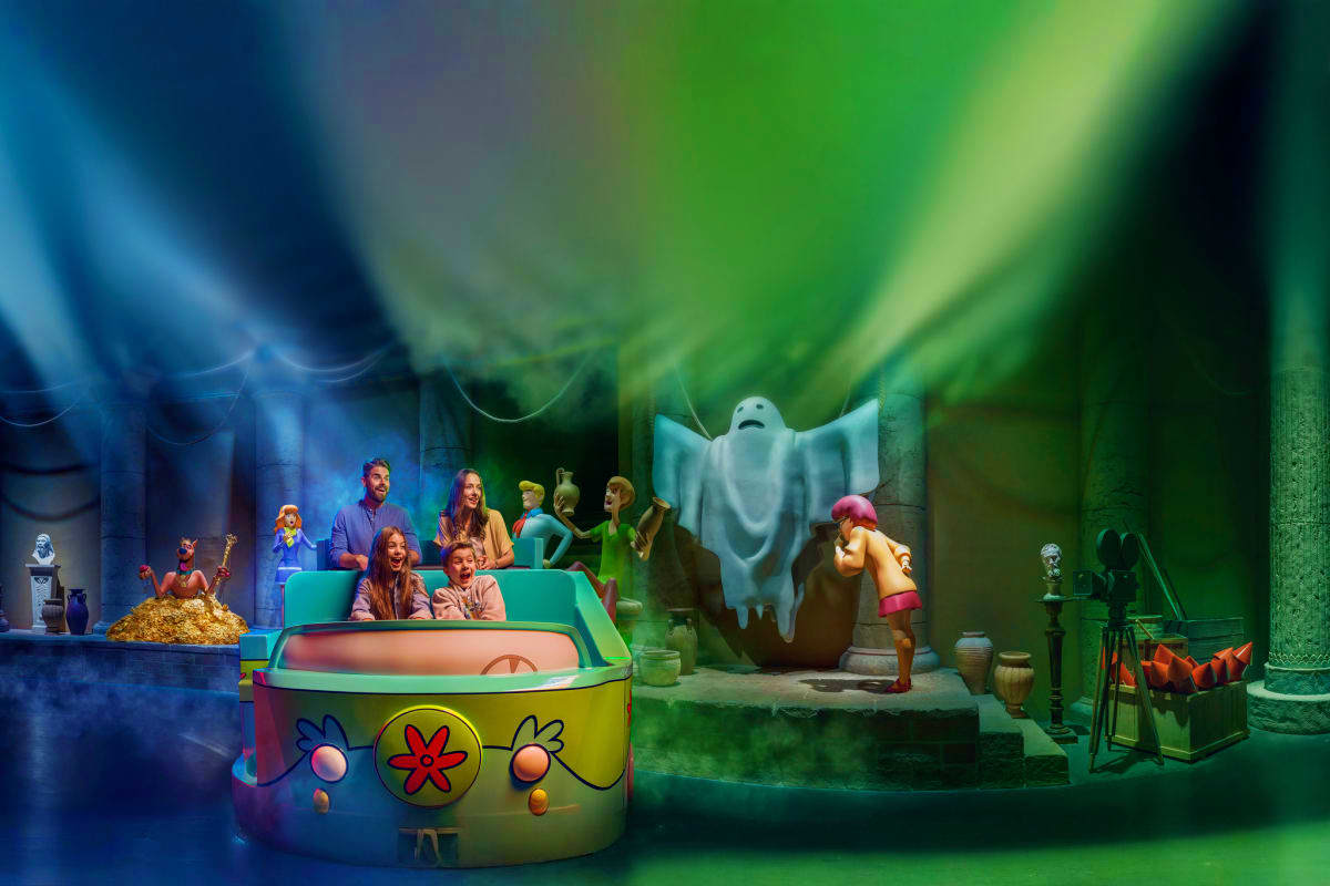 Theme park attraction scenes featuring colorful ride vehicles and costumed characters in front of spooky haunted house settin