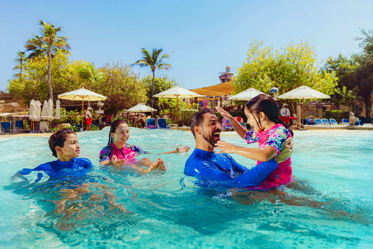 Wild Wadi Water Park Family enjoying water activities in turquoise pool at Wild Wadi Water Park with palm trees and white umbrellas in background