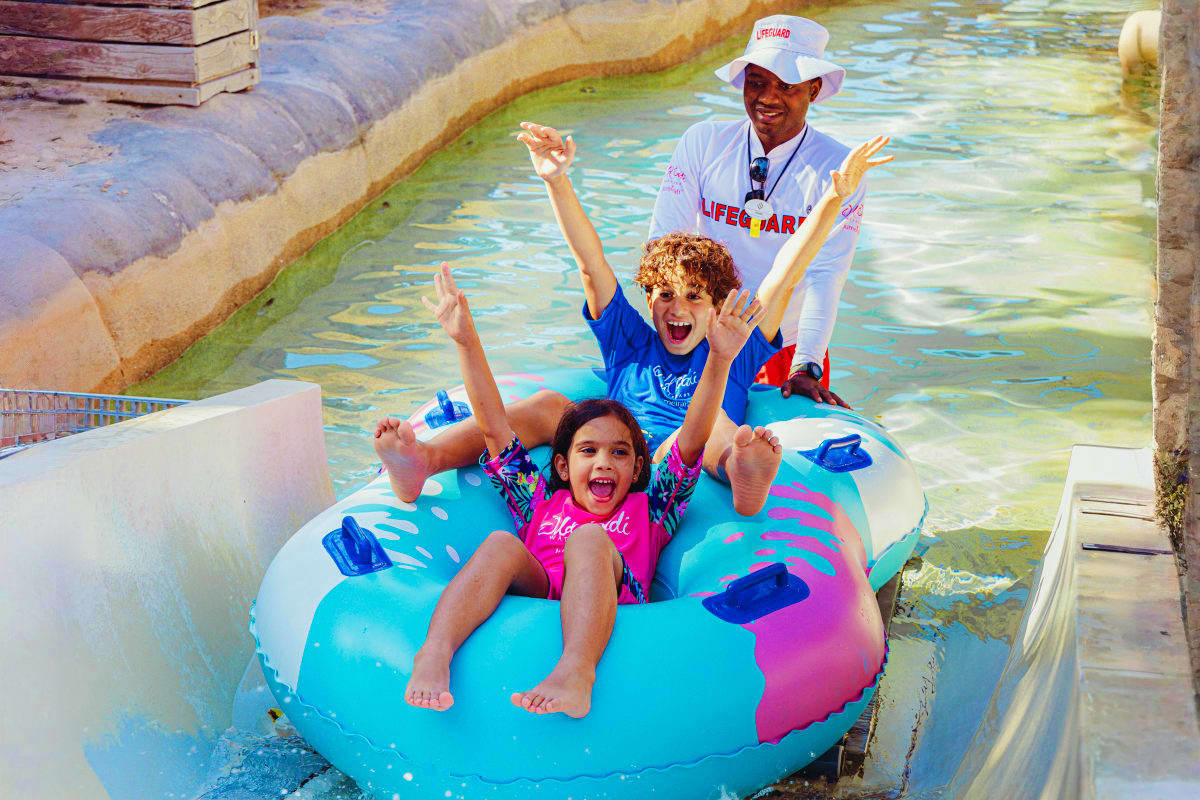 Wild Wadi Water Park Lifeguard supervising two children on a colorful inflatable raft ride in a shallow water channel at Wild Wadi Water Park