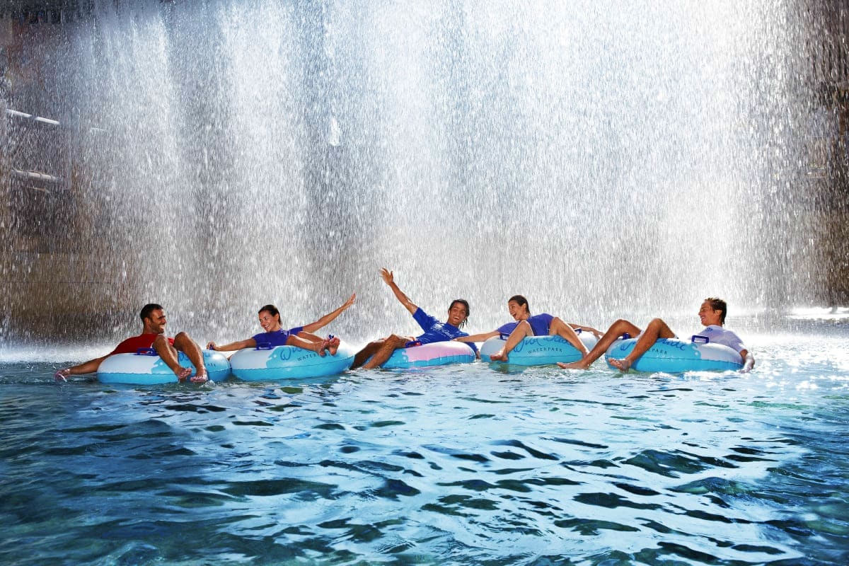 Wild Wadi Water Park Group of children on blue surfboards in ocean water with large waterfall cascade in background at Wild Wadi Water Park