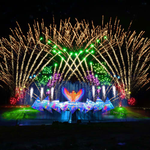 Grand stage with illuminated wings design, colorful light beams, and pyrotechnics during Wings of Time night performance