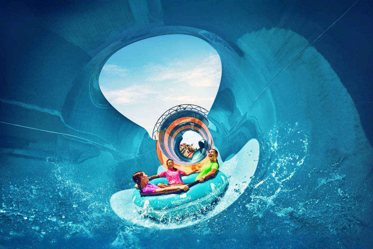 Yas Waterworld Three children on a turquoise inflatable raft splashing through a spiral water slide tunnel at Yas Waterworld, with blue wate