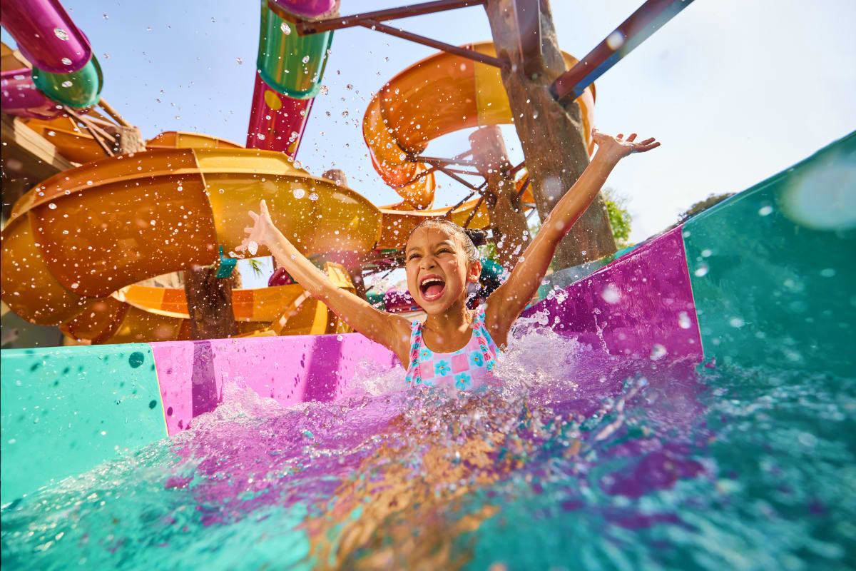 Yas Waterworld Child splashing down colorful water slide at Yas Waterworld theme park with orange and purple slide structures