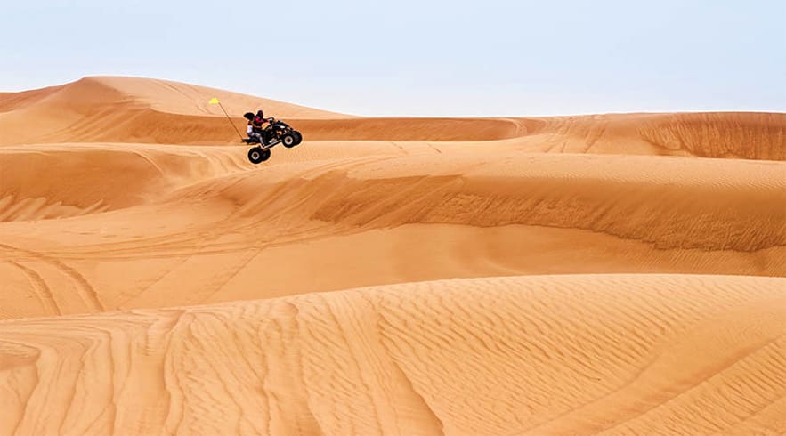 Rider performing stunt on quad bike jumping off sand dune in Abu Dhabi desert with golden sand dunes in background