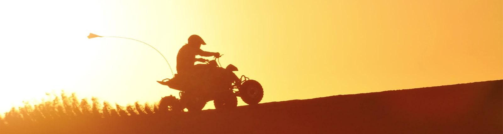 Silhouette of person riding ATV quad bike on desert dune at sunset in Abu Dhabi