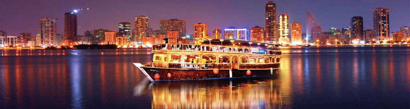 Dhow Cruise Abu Dhabi Illuminated traditional dhow boat on water at night with Abu Dhabi city skyline and lit buildings reflected in the bay