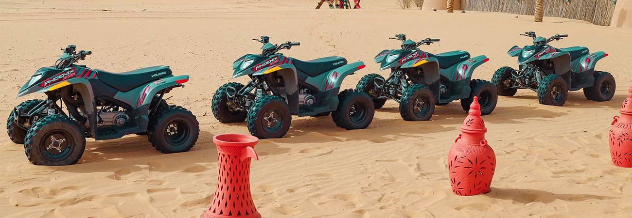 Row of turquoise and red ATVs lined up on sandy beach with red marker cones for desert safari tour