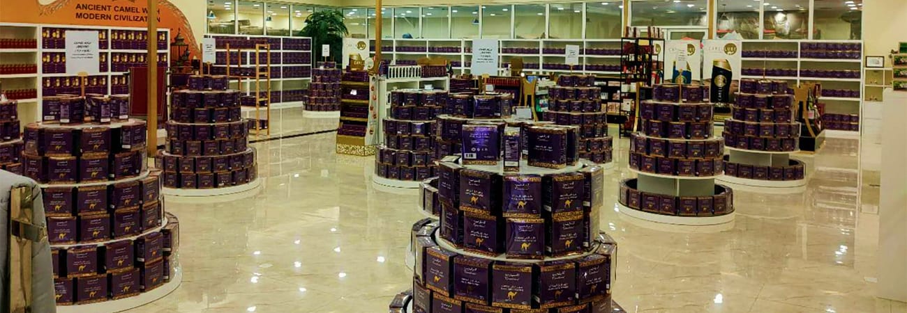 Guided Trip to Camel Farm Interior of camel dairy retail store displaying stacked dark purple containers of camel milk products on circular display sta