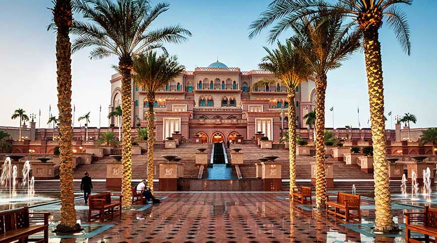 Emirates Palace courtyard with illuminated palm trees, fountain, and grand pink palace architecture in Abu Dhabi