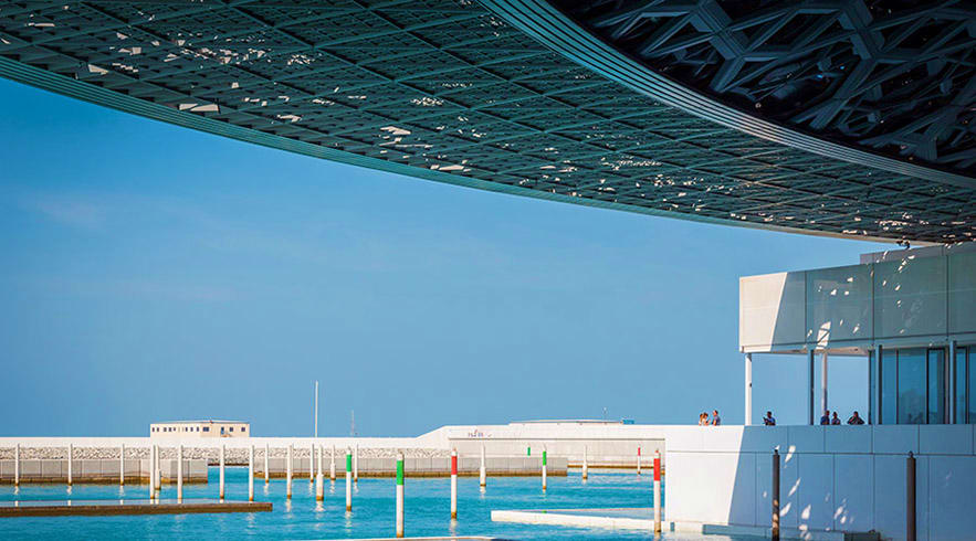 Modern waterfront architecture with turquoise water, white building structure, and colorful bollards at Abu Dhabi's waterside