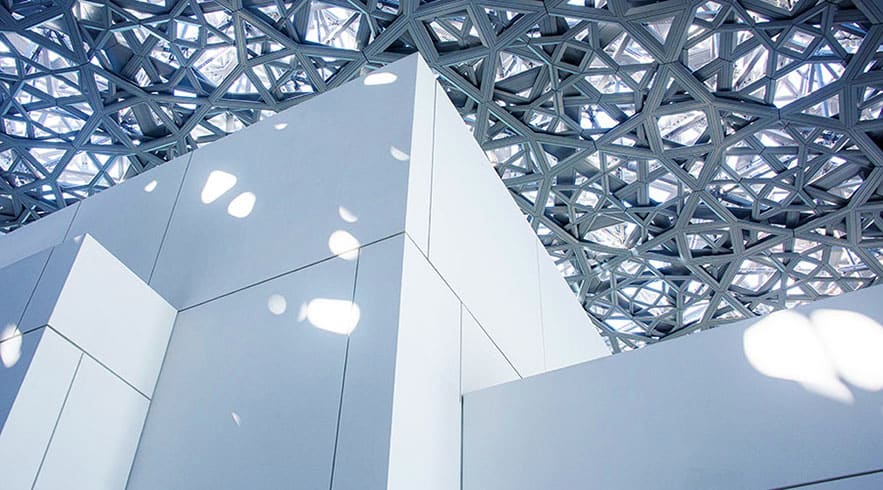 Interior view of Louvre Abu Dhabi with geometric white dome lattice ceiling and modern white architecture underneath
