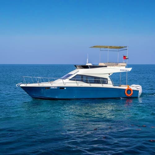 Blue and white motor yacht anchored in clear turquoise Mediterranean waters with canopy top and life ring visible