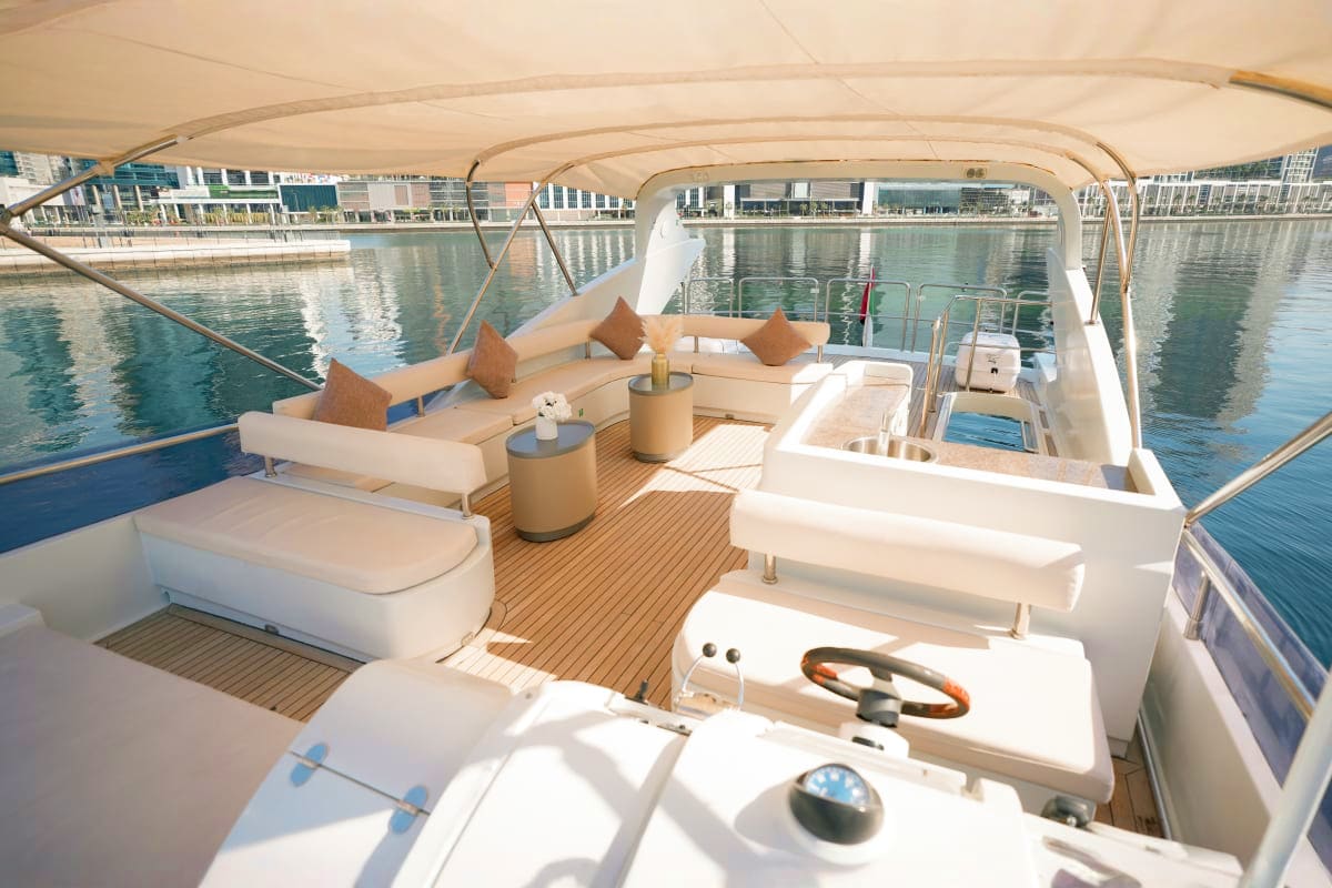 Gold X43 yacht deck with cream canopy, lounge seating, and helm station overlooking calm waterfront with modern buildings