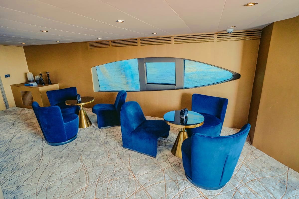 Stardom Luxury yacht lounge with blue velvet seating, brass accent tables, and panoramic ocean view windows on the Stardom