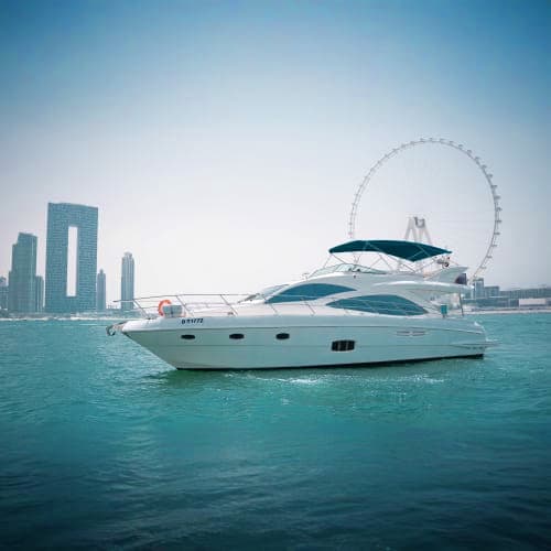 Luxury white motor yacht anchored in turquoise water with Dubai skyline and Ferris wheel in background