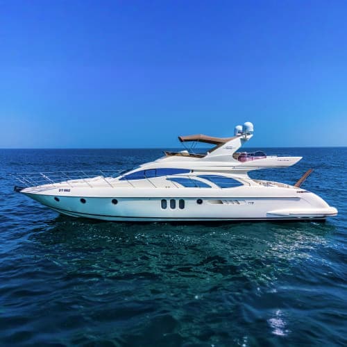 Luxury white motor yacht with blue stripe anchored in clear blue ocean water under sunny sky