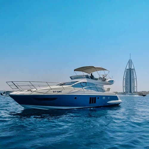 Luxury blue and white motor yacht anchored in turquoise water with Burj Al Arab sail-shaped hotel visible in background, Duba