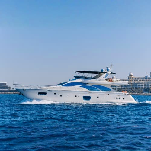 Luxury white and blue yacht with multiple decks moored in clear turquoise water near coastal buildings
