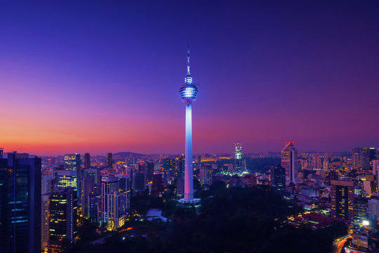 Kuala Lumpur cityscape at sunset with illuminated Menara Tower and surrounding skyscrapers against purple twilight sky