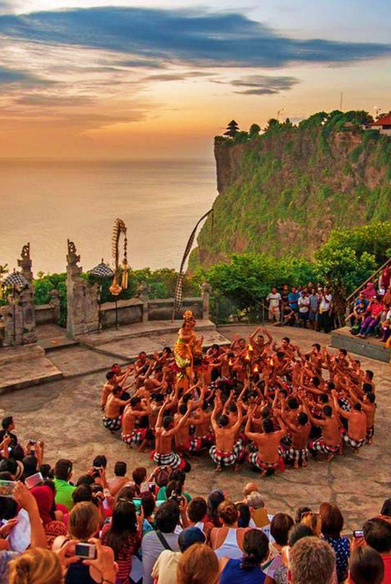 Traditional Balinese dance performance at Uluwatu Temple cliff overlooking the ocean at sunset with spectators watching
