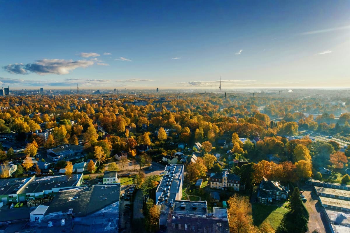 Aerial view of Riga's autumn landscape with golden trees, residential buildings, and city skyline with church spires in the d