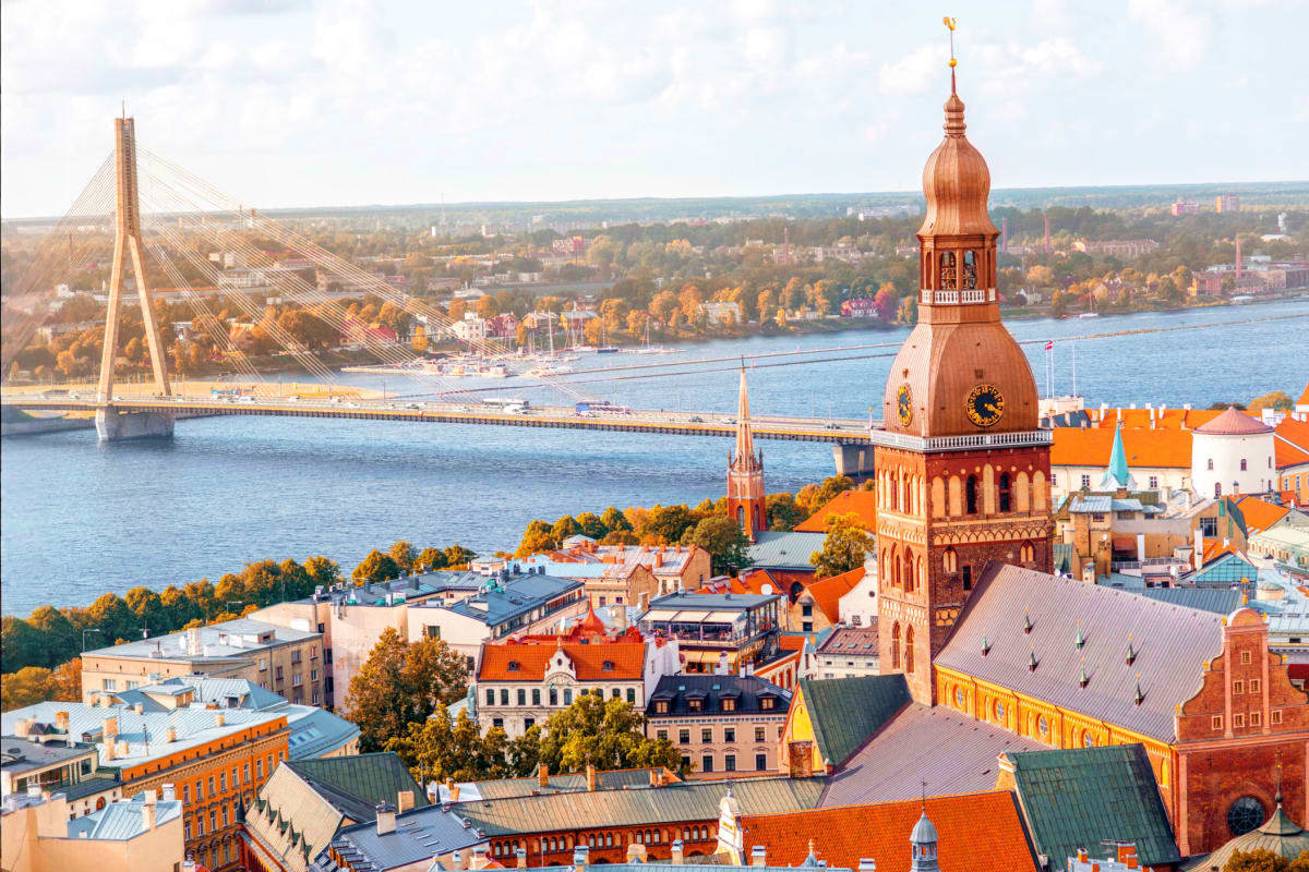 Aerial view of Riga, Latvia showing the Daugava River, cable-stayed bridge, historic cathedral dome, and autumn foliage