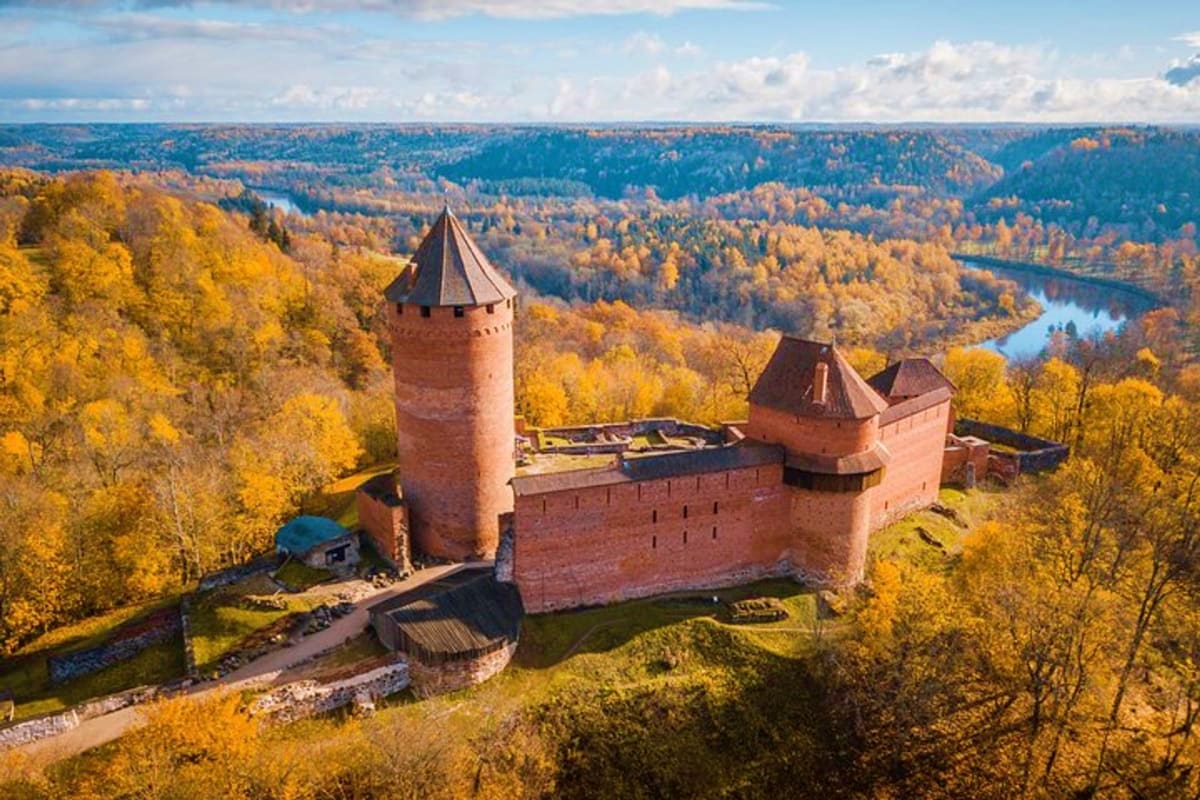 Medieval brick castle with towers surrounded by autumn forest and winding river in Latvia
