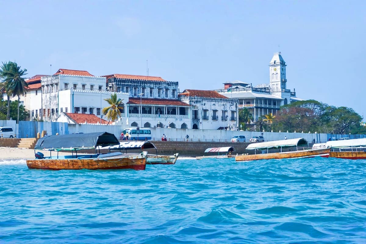 Waterfront view of Stone Town Zanzibar with historic white colonial buildings, clock tower, traditional wooden boats in turqu