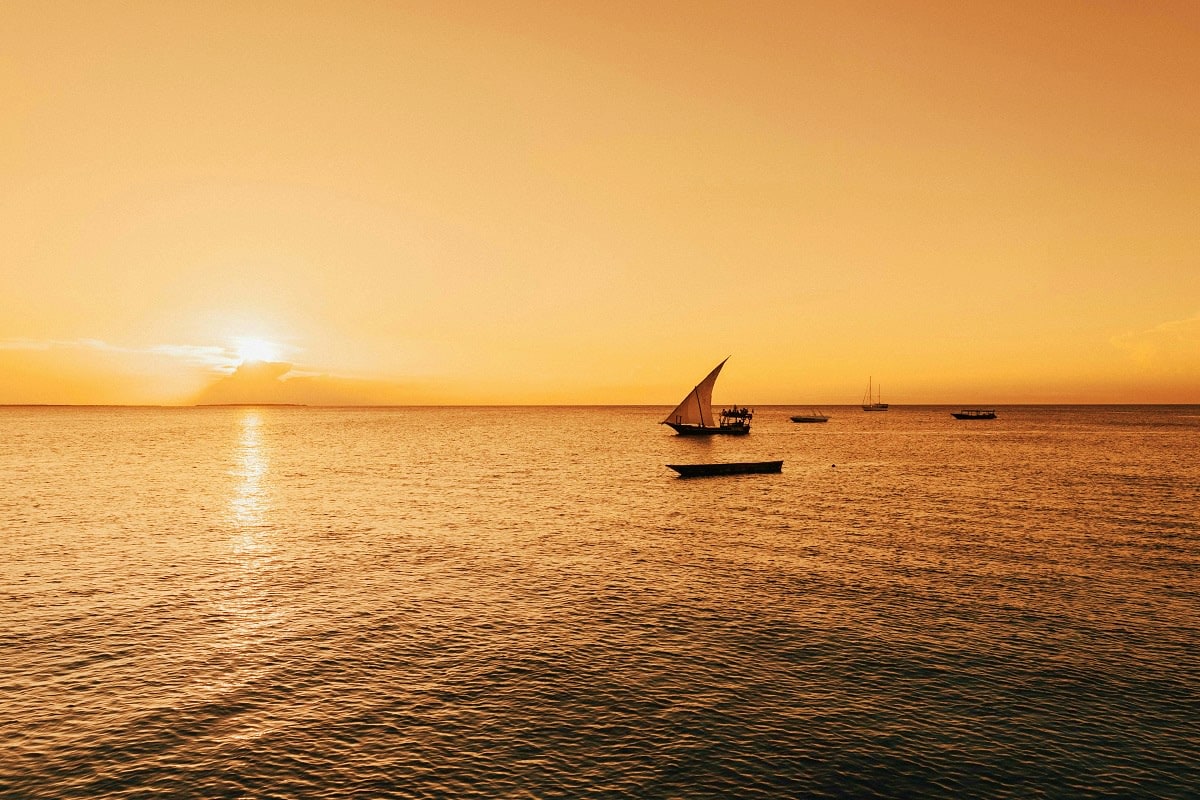 Traditional dhow sailboat on calm ocean waters at golden sunset in Zanzibar