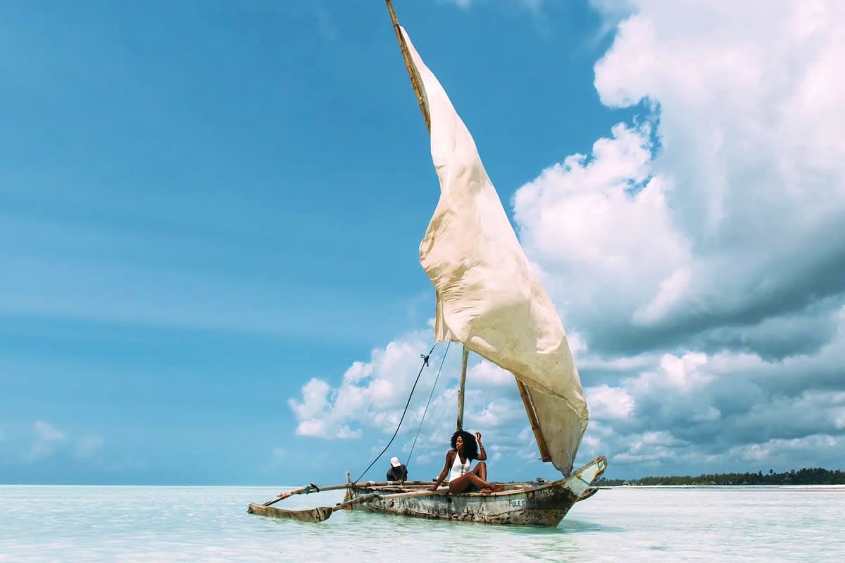 Traditional wooden sailing dhow with white sail on turquoise Indian Ocean waters near Zanzibar coastline under blue sky with 