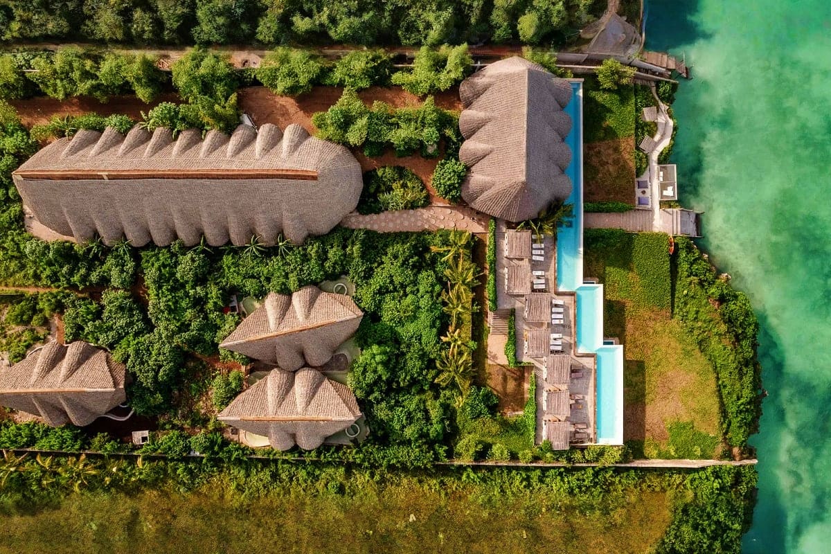 Aerial view of luxury beachfront resort with distinctive shell-shaped buildings surrounded by tropical vegetation and turquoi