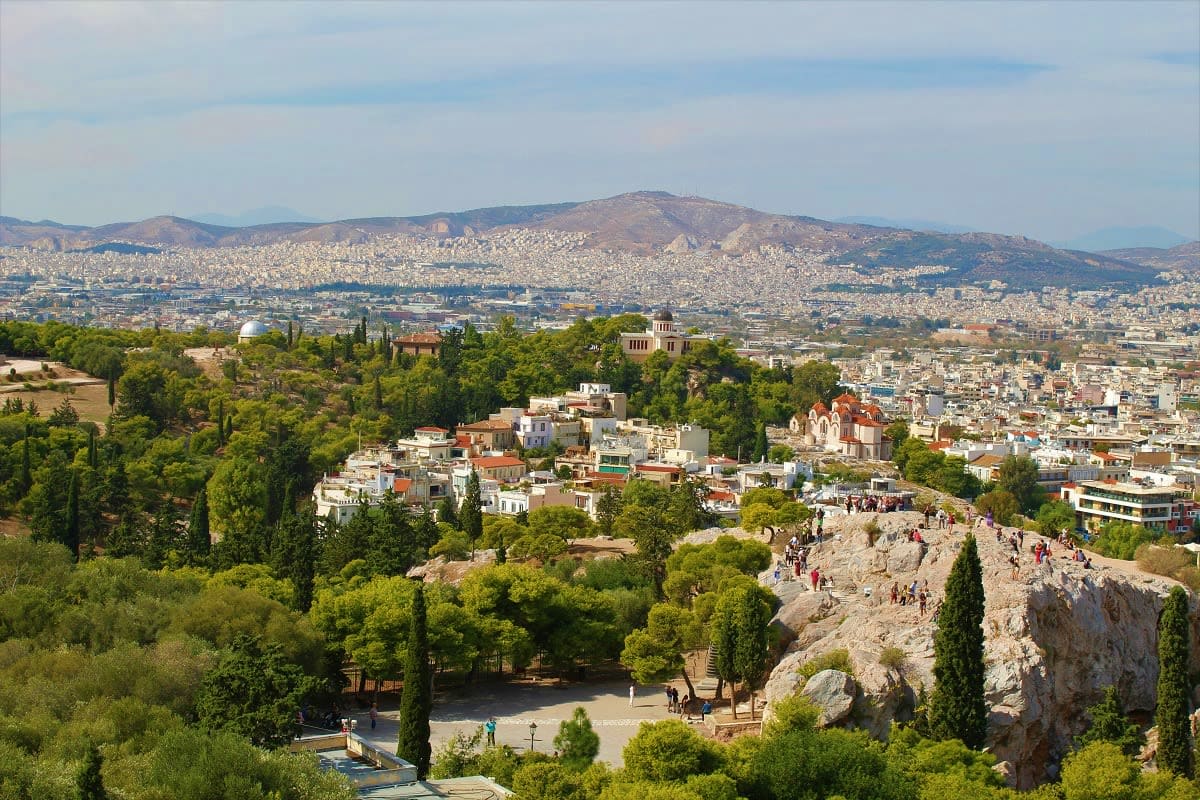 Aerial view of the Acropolis ruins with tourists, surrounded by cypress trees and residential neighborhoods, Athens cityscape