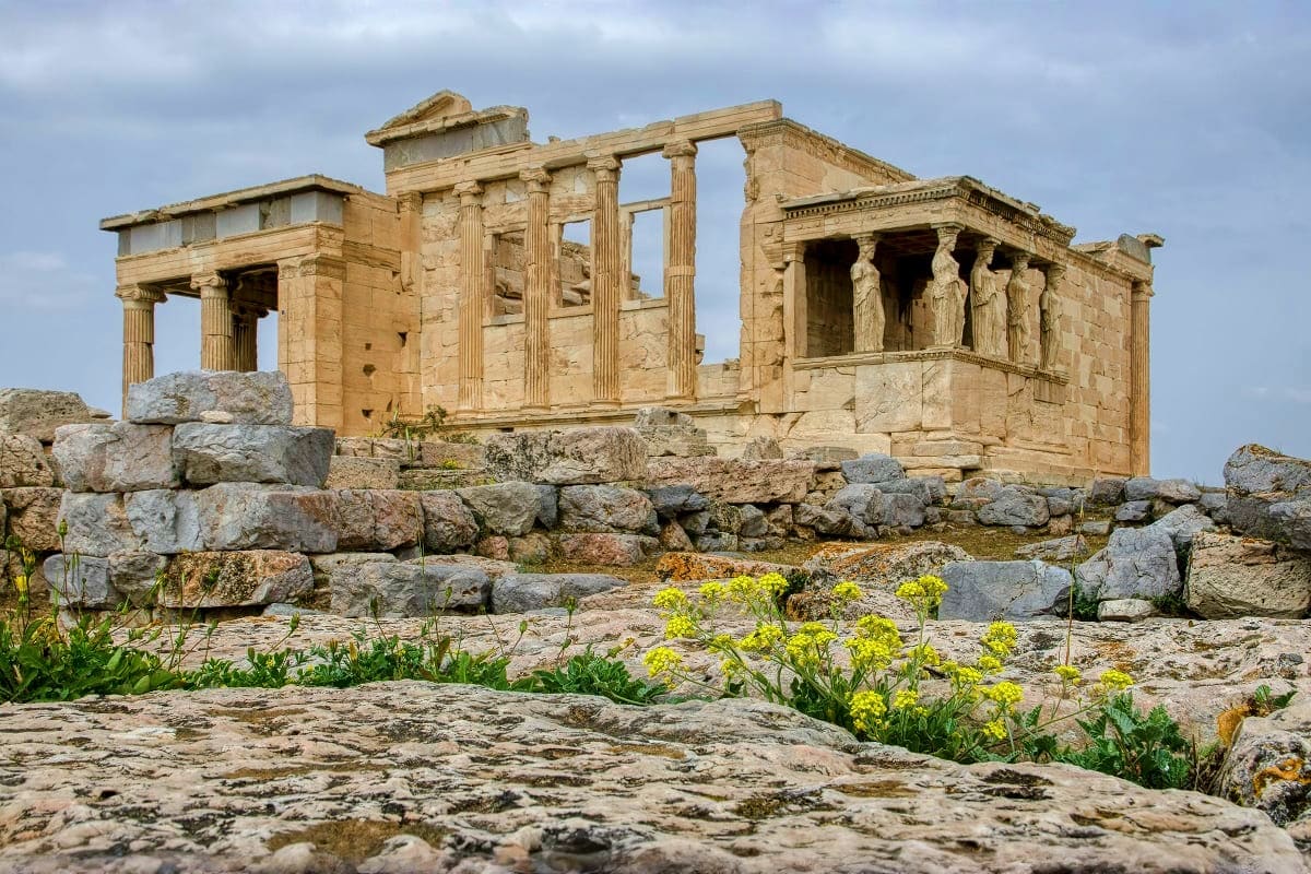 Ancient Greek temple ruins with Ionic columns and caryatid statues on the Acropolis in Athens, surrounded by stone ruins and 