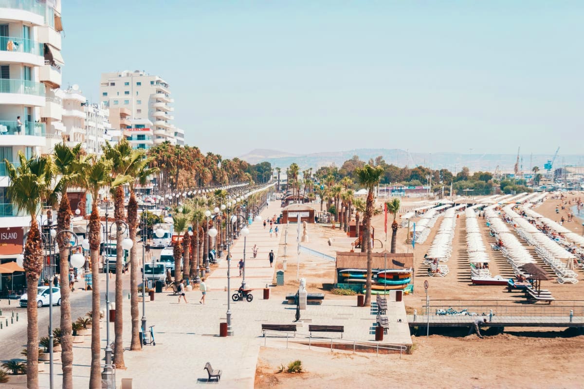 Beachfront promenade in Cyprus with palm trees, sandy beach, modern white apartment buildings, and Mediterranean Sea view