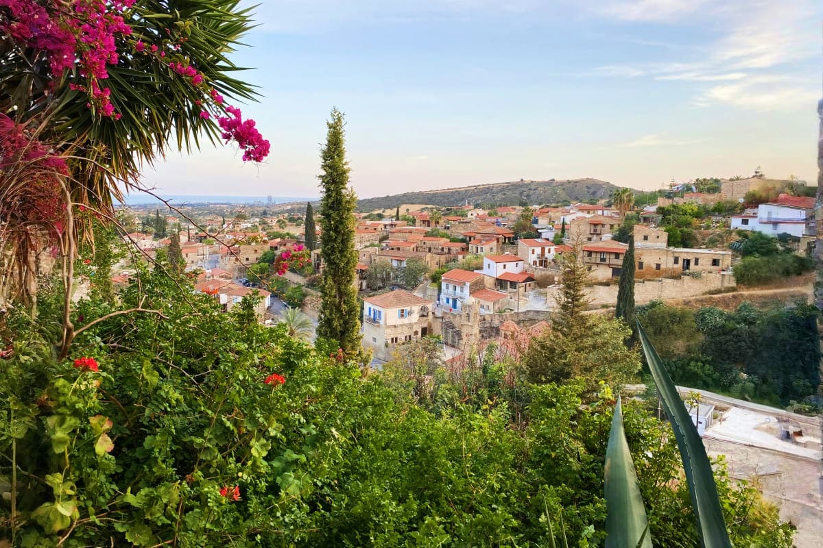 Panoramic view of a traditional Cypriot village with terracotta roofs nestled in hillside landscape, framed by vibrant pink b