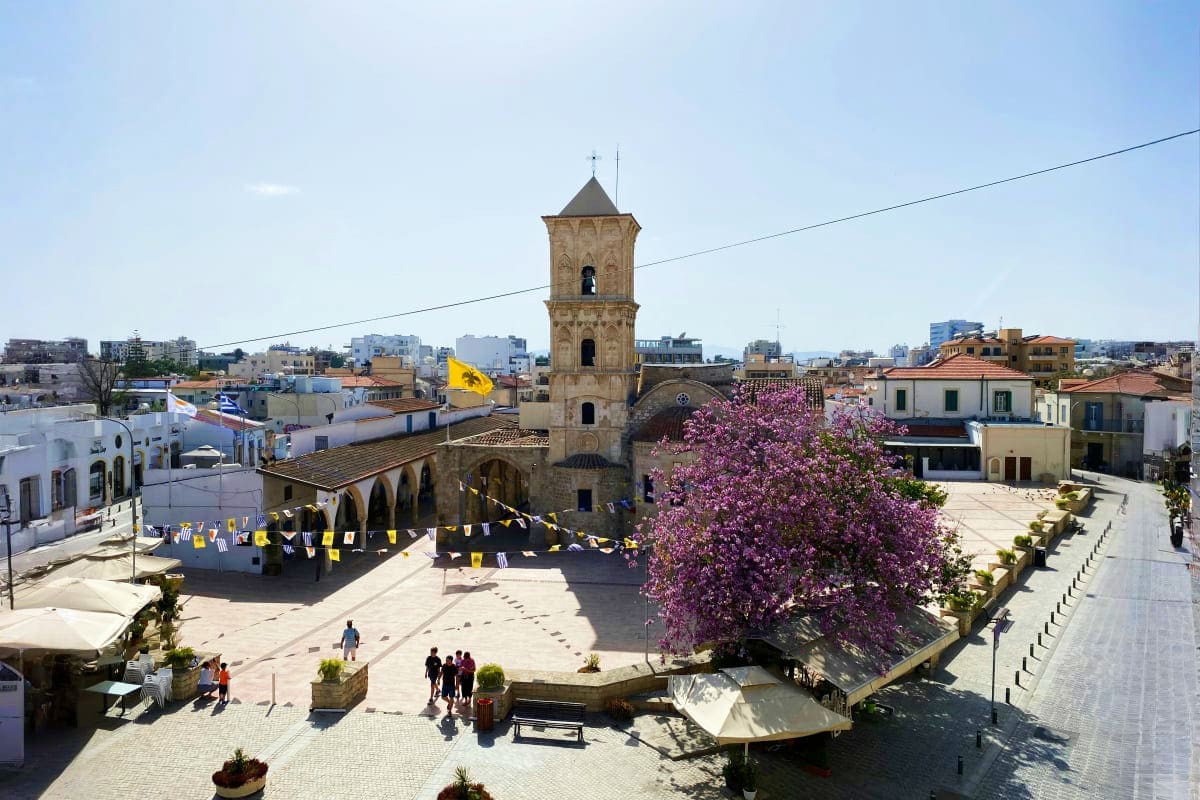 Historic town square in Larnaca, Cyprus with stone bell tower, blooming bougainvillea, and traditional Mediterranean architec