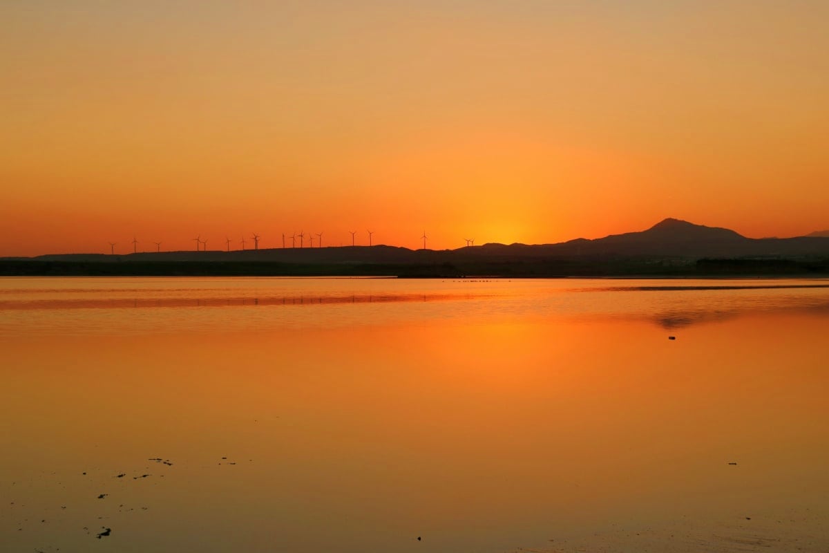 Sunset over calm bay with wind turbines silhouetted on distant hills and mountains in Cyprus