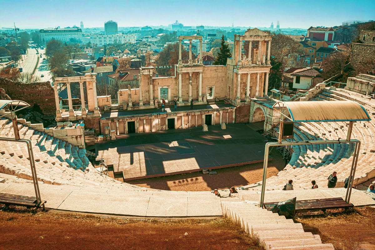 Roman theater ruins in Plovdiv with ancient stone columns and stage overlooking modern city skyline in Bulgaria