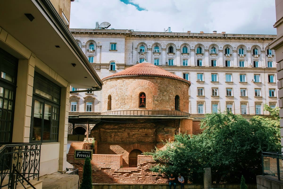 Medieval red brick church with terracotta roof nestled in courtyard between modern white apartment buildings in Sofia, Bulgar