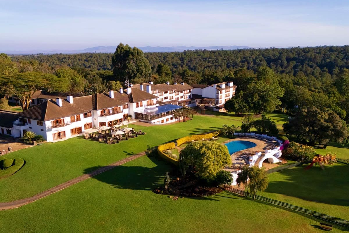 Aerial view of Grand Kenya luxury resort with white buildings, manicured grounds, blue swimming pool, and surrounding forest 