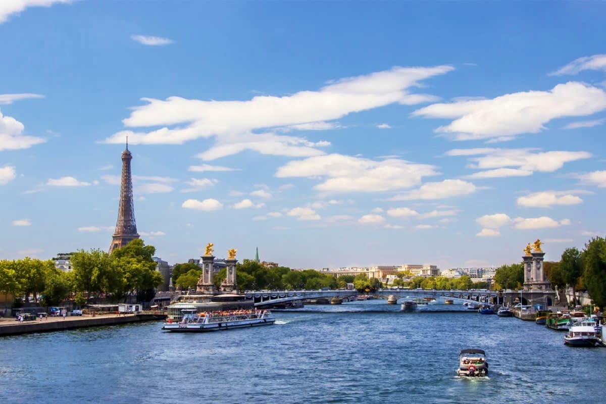 Eiffel Tower and Seine River with tourist boats and Pont de l'Alma bridge in Paris under blue sky with white clouds