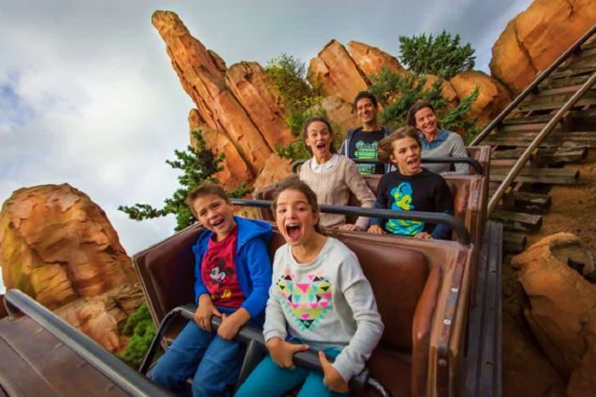 Children riding a roller coaster through rocky terrain at a theme park attraction