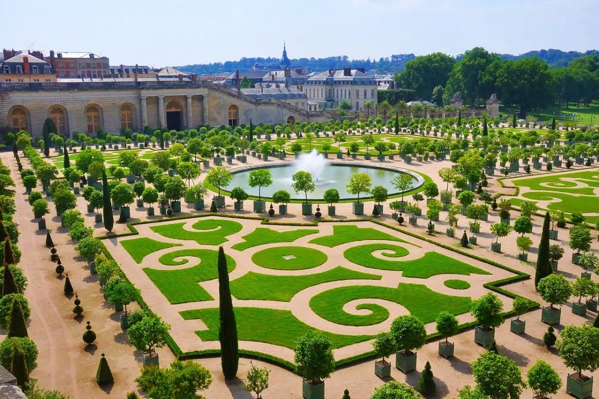Aerial view of the formal gardens at Palace of Versailles with manicured lawns, geometric hedges, circular fountain, and clas